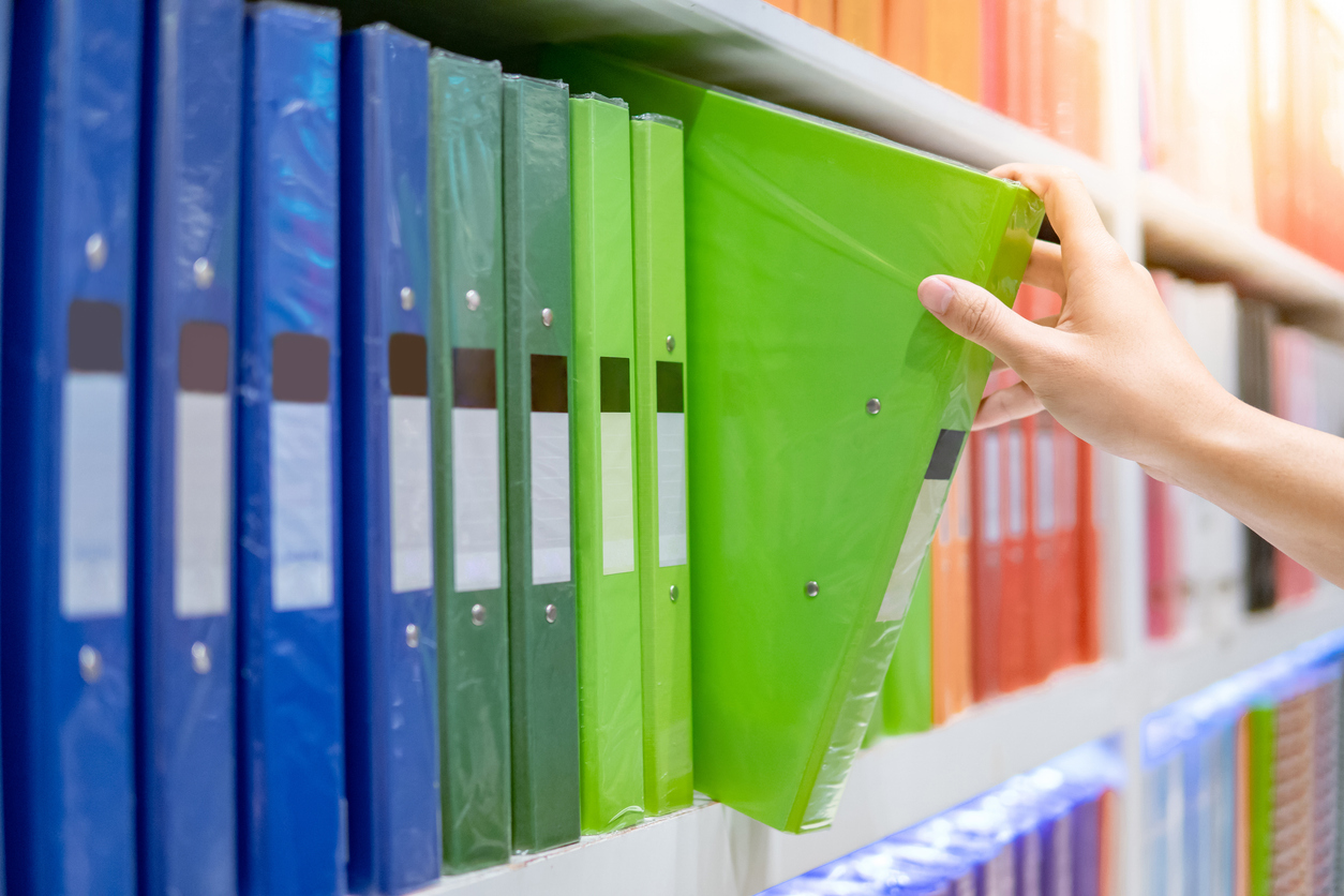 A hand takes a green binder off a shelf