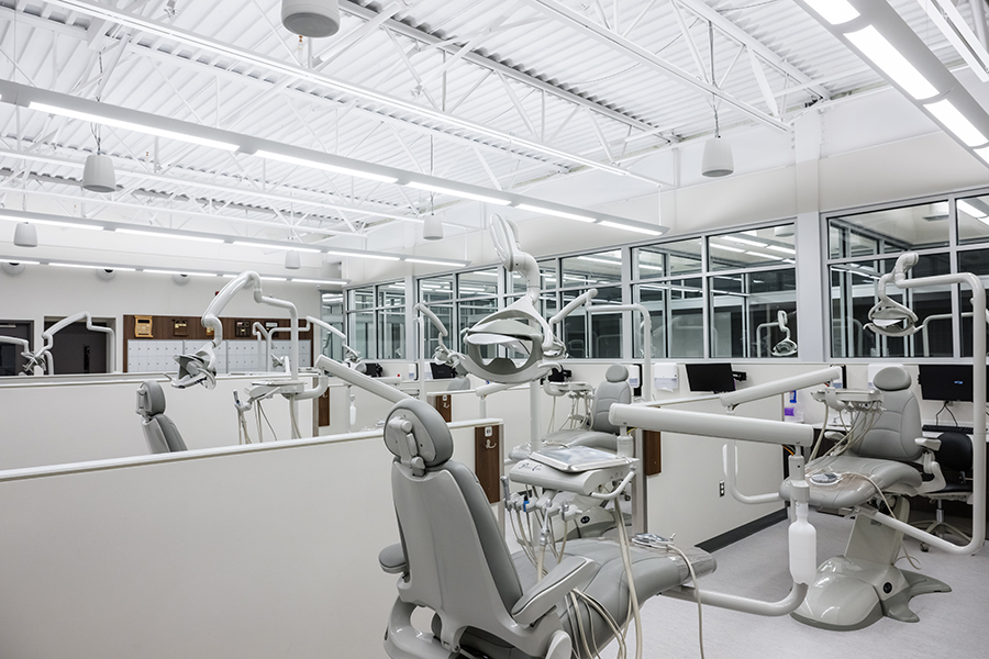 Interior view of a bright, modern dental lab with multiple gray dental stations, each equipped with chairs, lights, and dental tools.